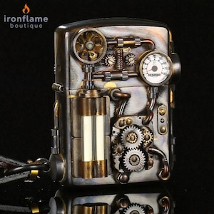 Peut inclure: Briquet de style steampunk avec des engrenages, jauges et tuyaux complexes en tons bronze et argent. Le briquet a un design rectangulaire avec une esth&eacute;tique m&eacute;canique d&eacute;taill&eacute;e, et la marque "ironflame boutique" est visible.