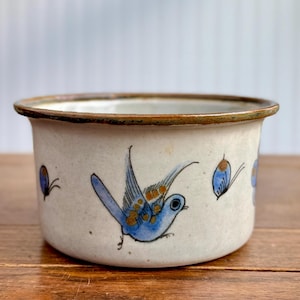 May include: A white ceramic mug with a black handle and the text "But First, Coffee" in a bold, black font. The mug is set against a blurred background, suggesting a cozy setting.