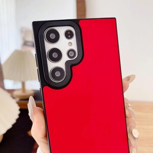 May include: A red and black phone case with a camera module cutout. The case has a glossy red finish on the right side and a black camera module area with multiple camera lenses. The phone case is designed to protect the phone.