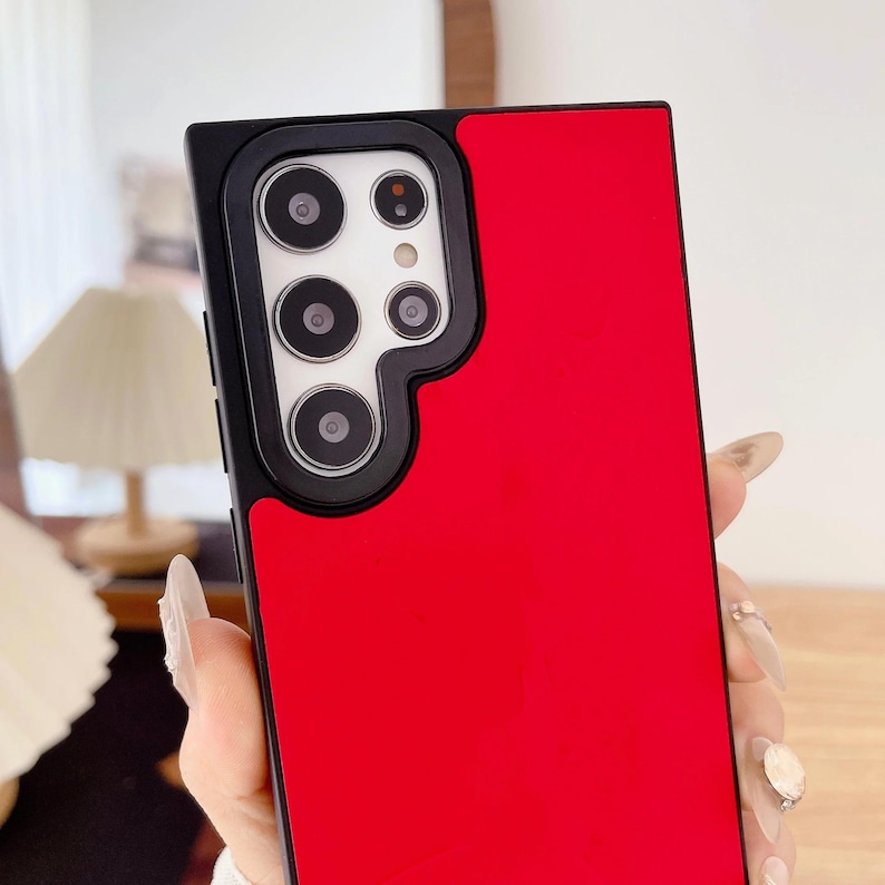May include: A red and black phone case with a camera module cutout. The case has a glossy red finish on the right side and a black camera module area with multiple camera lenses. The phone case is designed to protect the phone.