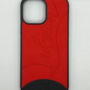 May include: A red phone case with a black border and base. The case features the embossed cursive text "Louboutin" in a lighter shade of red. The bottom of the case has the text "Christian Louboutin PARIS".