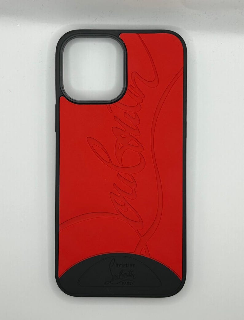May include: A red phone case with a black border and base. The case features the embossed cursive text "Louboutin" in a lighter shade of red. The bottom of the case has the text "Christian Louboutin PARIS".