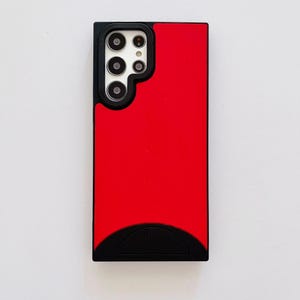 May include: A red and black phone case. The case has a rectangular shape with a red center and black borders. The top left corner features a cutout for the phone's camera, with multiple circular lenses. The bottom has a curved black section.