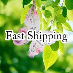 May include: A butterfly-shaped hanging ornament made of white paper with a pink floral pattern. The ornament features the printed text "LOVE GROW" and is suspended by a piece of twine. The butterfly has a die-cut shape with visible pink petals.