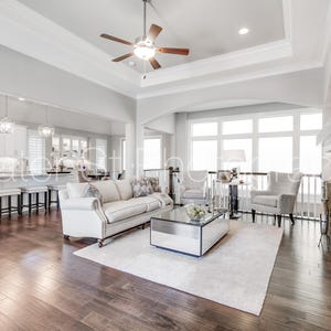 May include: A spacious living room with hardwood floors, a white sofa, and two armchairs. A mirrored coffee table sits on a white rug. The room features a stone fireplace and large windows, creating a bright and airy atmosphere.