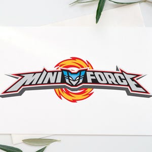 May include: A white greeting card featuring the text "MINI FORCE" in a stylized, bold font with red, gray, and black accents. The logo includes a blue and white emblem set against a fiery orange and yellow background.