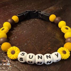 以下が含まれることがあります： 白い文字ビーズで「SUNNY」と書かれた犬の首輪。 首輪には、黄色のヒマワリと丸いビーズ、茶色のビーズが付いています。 首輪には黒いバックルが付いています。