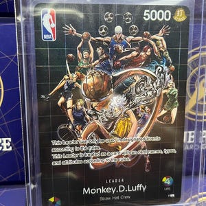 May include: A One Piece card featuring Monkey.D.Luffy of the Straw Hat Crew, with an NBA logo. The card has a black background with basketball players and the number 5000. Text on the card includes "STRIKE" and game rules.