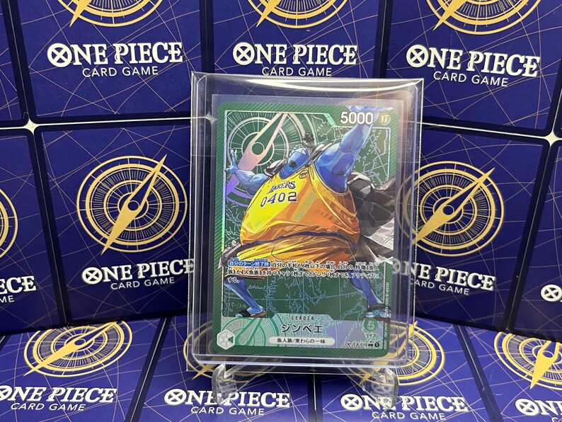 May include: A One Piece card featuring a blue-skinned character in a yellow and orange basketball jersey with the number 0402. The card is in a protective sleeve, with a green and white design. The background shows other One Piece card game cards.