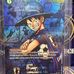 May include: A One Piece trading card featuring Monkey D. Luffy wearing a blue jersey and hat, holding a football. The card has a blue holographic finish, a power level of 7000, and text including Double Attack and On Play instructions.