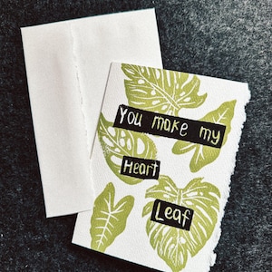 May include: A handmade greeting card with a white envelope. The card features green leaf prints and the text "You make my Heart Leaf" in black. The card has a torn edge, giving it a rustic look.