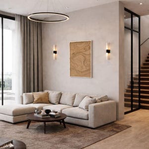 Puede incluir: Un salón moderno con un gran sofá seccional beige, una mesa de centro redonda y una alfombra marrón. La habitación cuenta con una lámpara circular, obras de arte y una escalera. Las paredes son de color claro y los pisos son de madera.