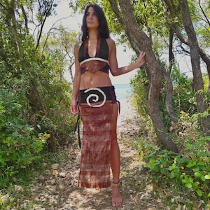 Puede incluir: Conjunto de dos piezas marrón compuesto por un top halter y una falda larga. El top es marrón oscuro con detalles blancos, y la falda tiene un diseño en espiral. El conjunto está hecho de una tela texturizada.