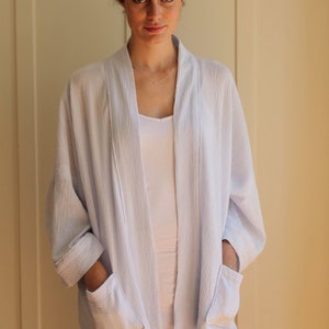 May include: A light blue, lightweight, open-front cardigan with long sleeves and two patch pockets. The cardigan is made of a soft, textured fabric.