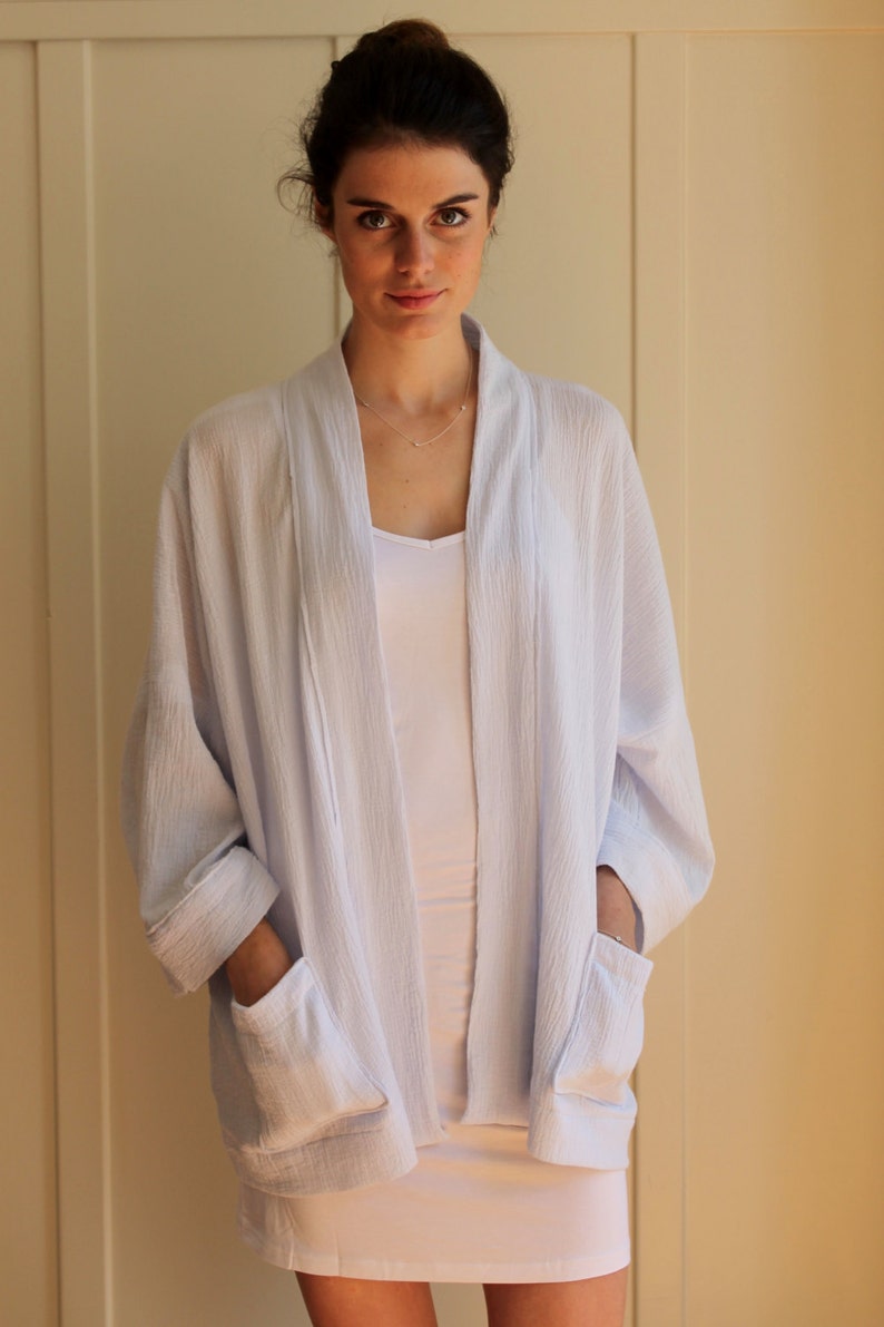 May include: A light blue, lightweight, open-front cardigan with long sleeves and two patch pockets. The cardigan is made of a soft, textured fabric.