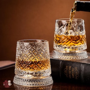 Peut inclure: Deux verres à whisky en cristal avec des motifs taillés en diamant. Un verre est rempli d'un liquide ambré provenant d'une bouteille sombre. Les verres reposent sur une base décorative, l'un sur un livre. Le fond est brun chaud.