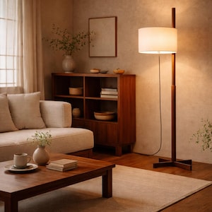 May include: A cozy living room scene with a wooden coffee table, a beige sofa, and a wooden cabinet. A floor lamp with a white lampshade illuminates the space. The room is decorated with vases and a neutral-colored rug.