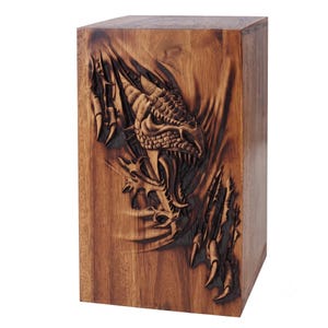 A wooden urn box carved with a 3D dragon face appearing to tear through the wood surface with claws.