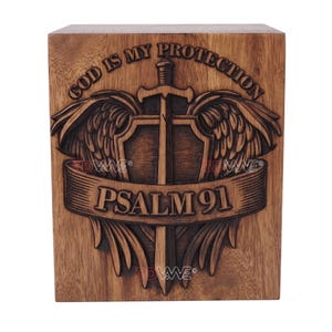 A wooden urn box carved with a sword, feathered wings, a shield, and the text PSALM 91 and GOD IS MY PROTECTION.