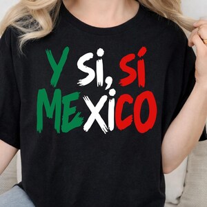 Può includere: Una t-shirt nera a maniche corte con il testo Y SI, SÍ MEXICO stampato in un carattere stile pennellata. Le lettere sono colorate in verde, bianco e rosso, richiamando i colori della bandiera messicana, con un design grafico audace.