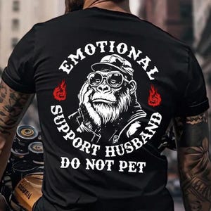 May include: Black t-shirt with a graphic of a gorilla wearing glasses and a hat, with the text "EMOTIONAL SUPPORT HUSBAND DO NOT PET" in a circular design. Red flame graphics are on either side of the gorilla.