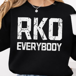 Puede incluir: Sudadera negra con el texto blanco "RKO EVERYBODY". Las letras tienen un efecto agrietado y desgastado. La sudadera es de color negro liso.