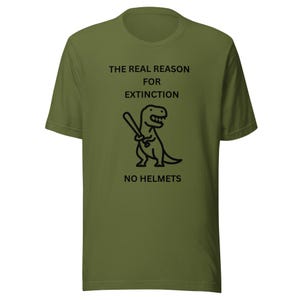 May include: An olive green short-sleeve t-shirt featuring a black graphic of a Tyrannosaurus Rex holding a baseball bat. The text printed in black reads: THE REAL REASON FOR EXTINCTION NO HELMETS. The shirt has a crew neckline and a standard fit.