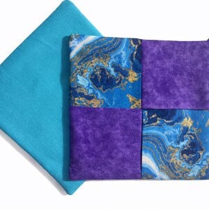 May include: A square, quilted pot holder with a loop for hanging. The pot holder is made of four squares: two solid purple and two with a blue and gold marbled pattern. A turquoise square is next to the pot holder.