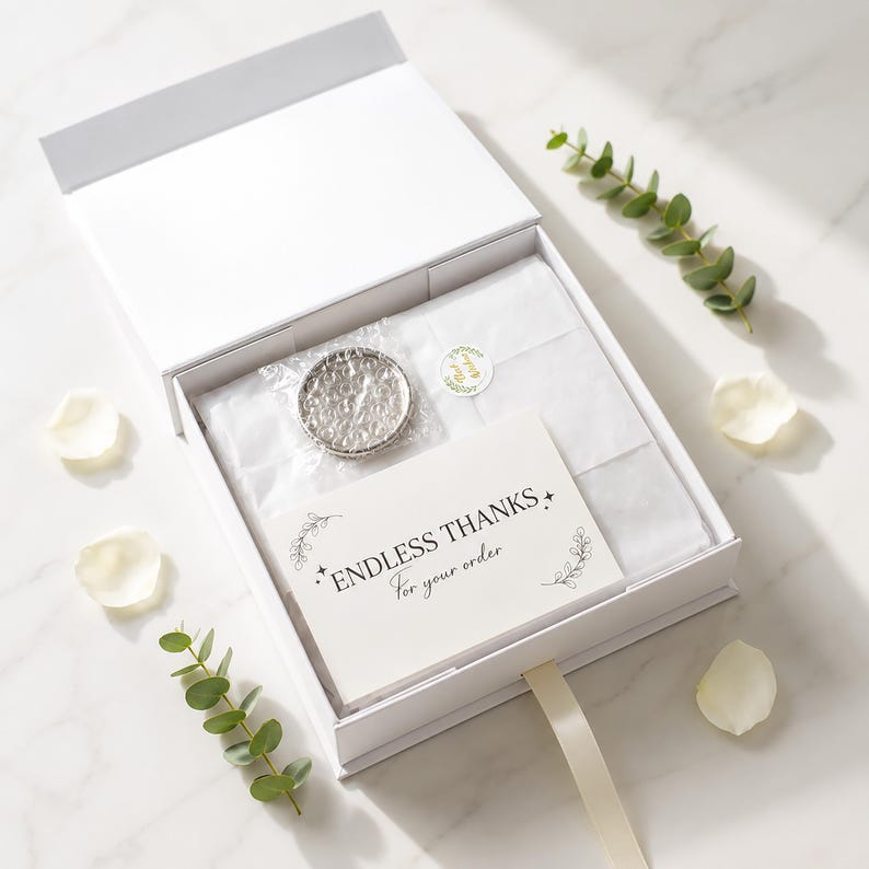 Puede incluir: Una caja de regalo blanca con tapa magn&eacute;tica que contiene papel de seda blanco, un peque&ntilde;o objeto circular envuelto en pl&aacute;stico de burbujas y una tarjeta rectangular con el texto ENDLESS THANKS For your order impreso en negro.