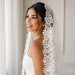 Puede incluir: Un velo de novia blanco y transparente con un intrincado borde de encaje floral. El delicado patr&oacute;n de encaje presenta bordes festoneados y bordados detallados, que caen suavemente sobre la cabeza y los hombros como un accesorio de boda cl&aacute;sico.