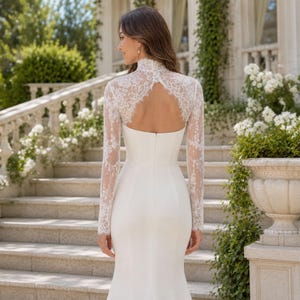 May include: A floor-length white gown featuring long lace sleeves and a high lace neckline. The bodice includes a keyhole back design with a row of small buttons at the neck, transitioning into a smooth, solid white skirt that flows to the floor.