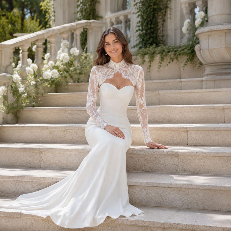 May include: A floor-length white gown featuring a sweetheart neckline and a fitted bodice. The dress includes a high-neck lace overlay with long sleeves that covers the shoulders and upper chest, transitioning into a smooth, solid fabric skirt.