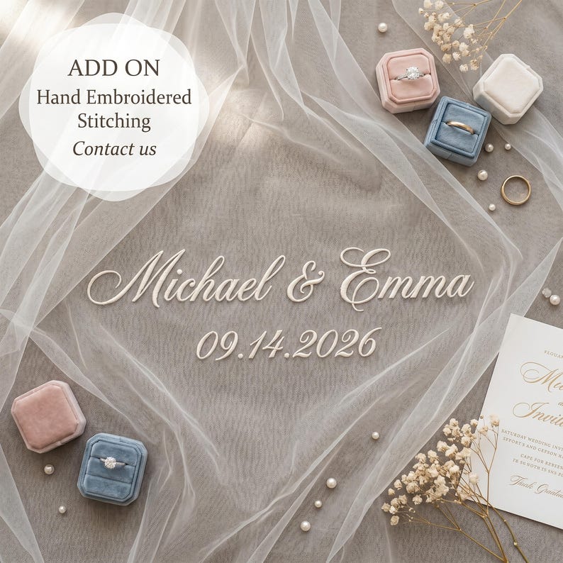 Puede incluir: Un arreglo de boda con texto en cursiva blanca que dice Michael & Emma 09.14.2026, rodeado de tela blanca transparente, cajas de terciopelo para anillos en rosa y azul, peque&ntilde;as perlas blancas, flores secas y una tarjeta de invitaci&oacute;n.