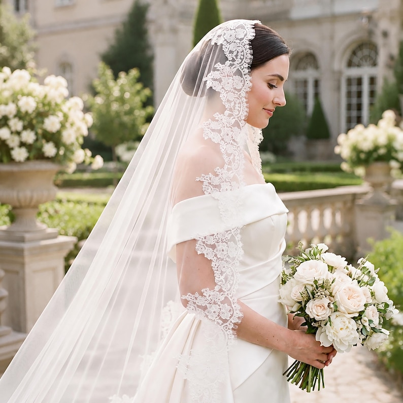 Puede incluir: Un velo de novia blanco hasta el suelo con un intrincado borde de encaje floral, usado sobre un vestido de sat&eacute;n blanco con hombros descubiertos. El velo es transparente y cae con elegancia, junto a un ramo de rosas blancas y follaje.