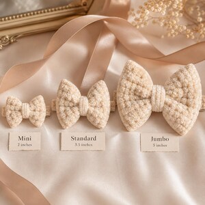 Puede incluir: Tres lazos para el cabello beige texturizados en varios tamaños: Mini (5,08 cm), Estándar (8,89 cm) y Jumbo (12,7 cm). Cada lazo está hecho de un material suave y afelpado y se muestra sobre una superficie de satén color crema. Los lazos están dispuestos en fila, mostrando sus diferentes tamaños.