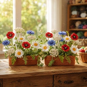 May include: Two crochet floral arrangements in rectangular brown baskets. The flowers include red poppies, white daisies, blue cornflowers, and white Queen Anne's lace. The arrangements sit on a wooden table in front of a window.