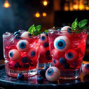 May include: Three glasses filled with a vibrant red cocktail, ice, and blueberries. Each glass is adorned with several eyeball-shaped candies, creating a spooky Halloween theme. Fresh mint sprigs add a touch of green.