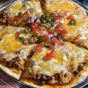 Può includere: Una pizza tagliata a fette, condita con formaggio giallo fuso, carne macinata, pomodori rossi a cubetti, cipolle rosse e jalapenos verdi. La crosta della pizza è visibile, con i condimenti distribuiti.