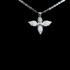 May include: A silver necklace with a pendant shaped like an angel. The angel pendant has outstretched wings and is covered in small, sparkling stones. The necklace chain is also silver and has a delicate, linked design. The background is black.
