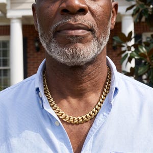 Mens Miami Cuban link chain in 18K gold plated stainless steel, worn on the neck of an older man on a brick porch.