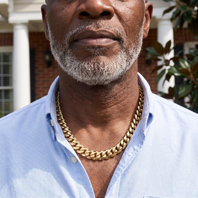 Mens Miami Cuban link chain in 18K gold plated stainless steel, worn on the neck of an older man on a brick porch.