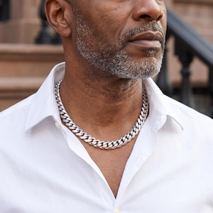 Mens Miami Cuban link chain in 925 silver plated stainless steel, worn on the neck of a man in his fifties outdoors in daylight.