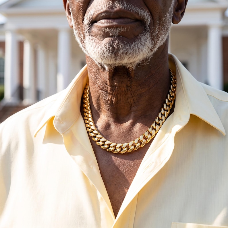 Mens Miami Cuban link chain in 18K gold plated stainless steel, worn on the neck of a man in his seventies in bright daylight.