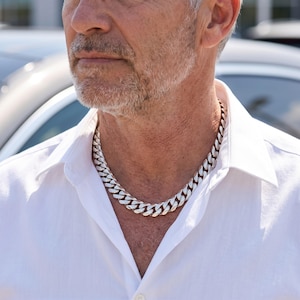 Mens Miami Cuban link chain in 925 silver plated stainless steel, worn on the neck of an older man outdoors in daylight.