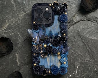 Op de afbeelding: Een decoratieve telefoonhoes met een blauw en zwart bloemenontwerp. De hoes heeft gebeeldhouwde rozen, vlinders en gouden accenten. De hoes is ontworpen voor een smartphone en heeft een camera-uitsparing.