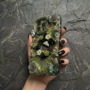 Op de afbeelding: Een decoratief telefoonhoesje met een wervelende geel-groene harsbasis, versierd met driedimensionale bloemaccenten in wit, groen en zwart, twee iriserende vlinderfiguren en een kleine centrale ronde spiegel.