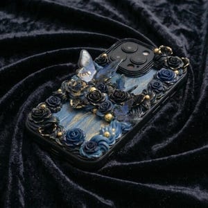 May include: Black phone case with a detailed floral and butterfly design. The case features blue and black roses, butterflies, and gold accents. The design is set against a blue and gold marbled background.