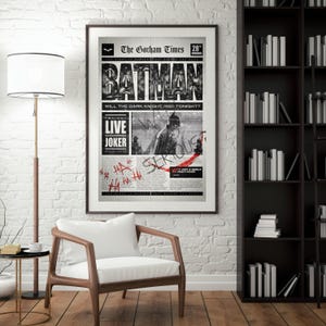 Może przedstawiać: Oprawiony czarno-biały plakat Batmana, stylizowany na stronę tytułową gazety. Nagł&oacute;wek "BATMAN" jest pogrubiony. Zawiera tekst "The Gotham Times" i "LIVE JOKER". Plakat jest w ciemnej drewnianej ramie.