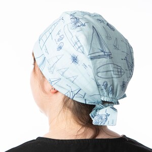 Peut inclure: Un bonnet de chirurgien bleu clair avec un imprimé de voiliers bleu et blanc. Le bonnet est noué à l'arrière de la tête.