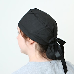 May include: A black scrub hat with a black ribbon tied at the back. The hat is made of a soft, comfortable fabric.